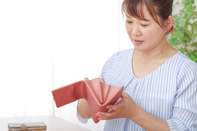 財布の中身を確認して困っている表情の主婦。生活費が足りない様子。