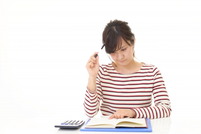 家計簿と電卓を前に悩む女性。破産後の生活再建に向けて考え込む様子